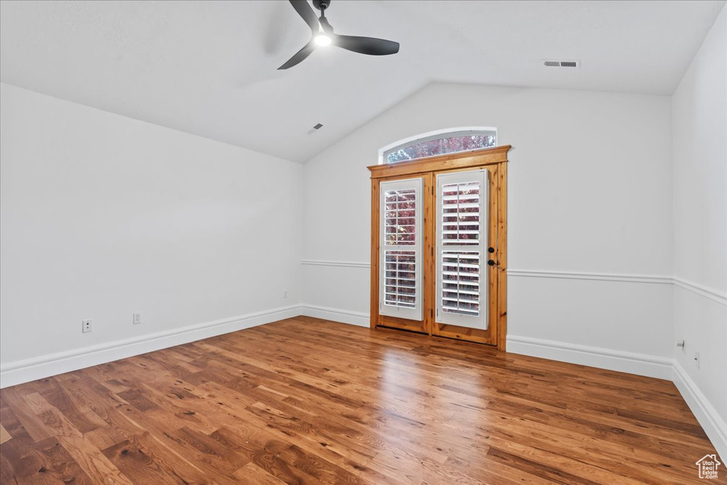Spare room featuring visible vents, wood finished floors, baseboards, a ceiling fan, and vaulted ceiling