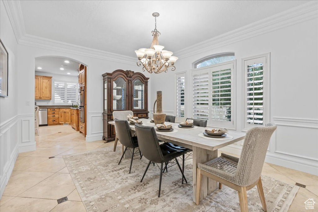 Dining area featuring ornamental molding, a decorative wall, a chandelier, arched walkways, and light tile patterned floors