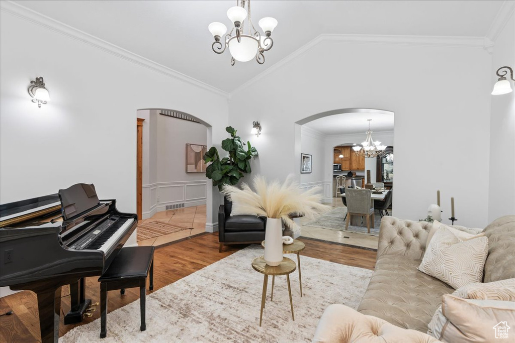 Living room with an inviting chandelier, ornamental molding, lofted ceiling, wood finished floors, and arched walkways