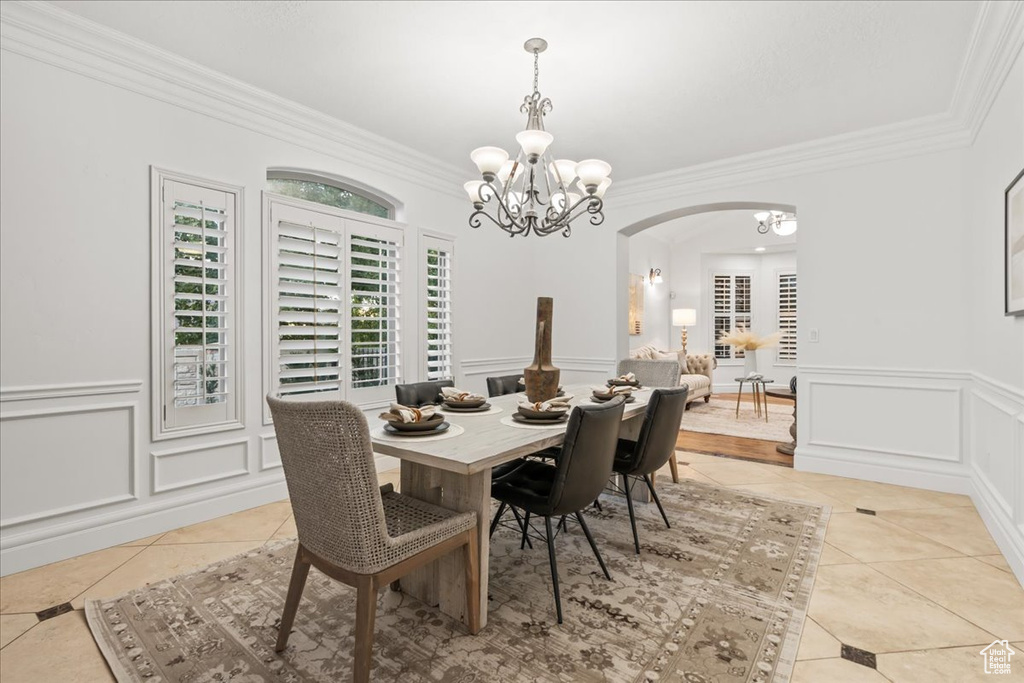 Dining space with crown molding, a decorative wall, arched walkways, a chandelier, and light tile patterned floors