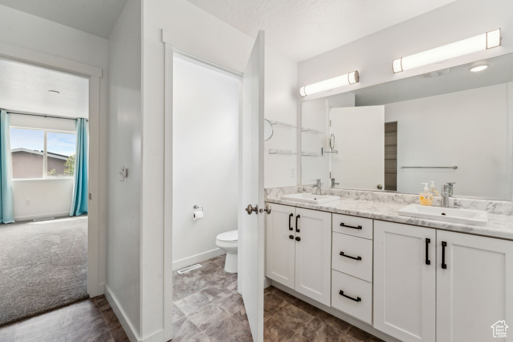 Bathroom with double vanity, toilet, baseboards, and a sink