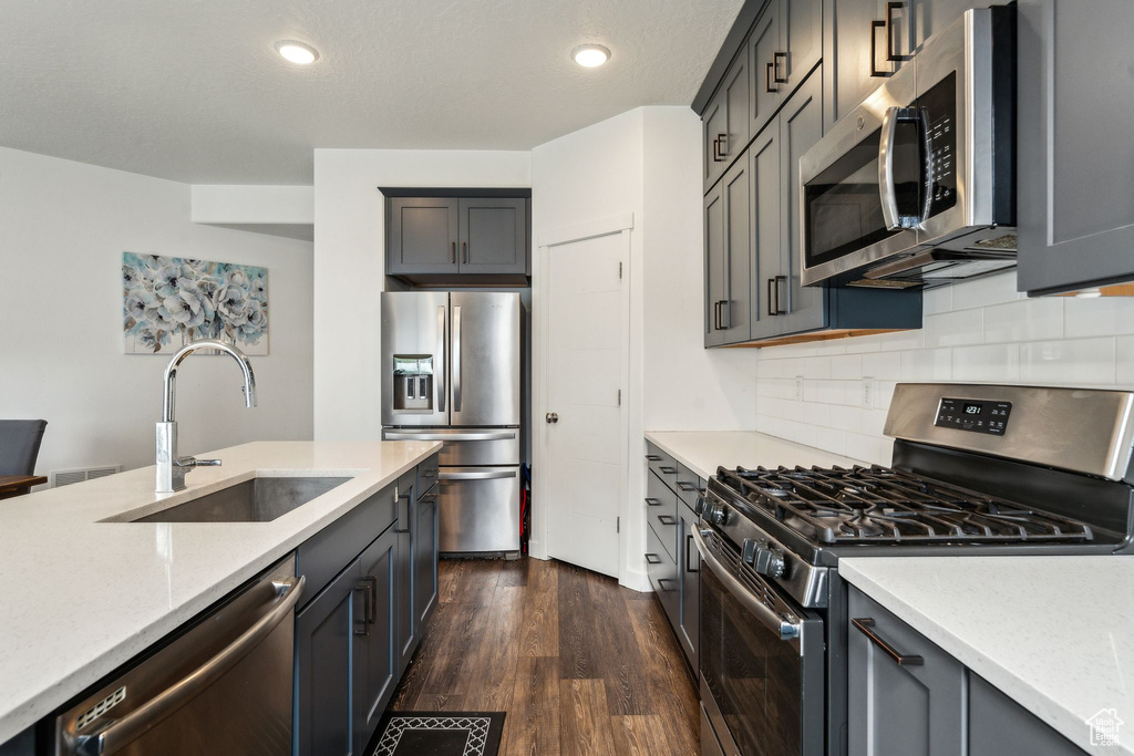Kitchen with light stone counters, a sink, dark wood finished floors, backsplash, and stainless steel appliances