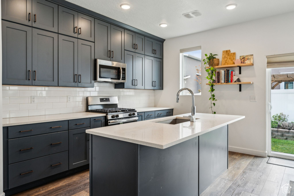 Kitchen featuring dark wood-type flooring, a sink, decorative backsplash, and appliances with stainless steel finishes