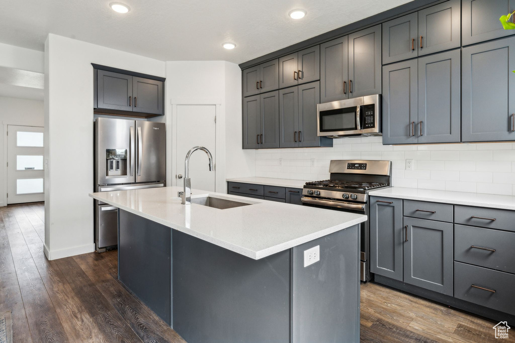 Kitchen featuring dark wood-style flooring, tasteful backsplash, a sink, light countertops, and stainless steel appliances