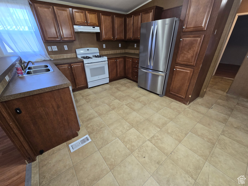 Kitchen featuring a sink, white gas range, freestanding refrigerator, under cabinet range hood, and visible vents