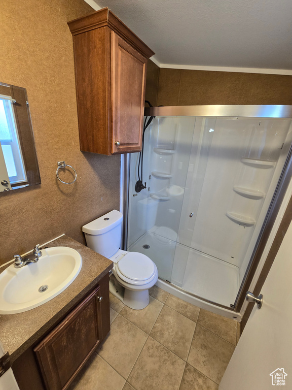 Bathroom with a textured wall, tile patterned flooring, vanity, toilet, and a stall shower