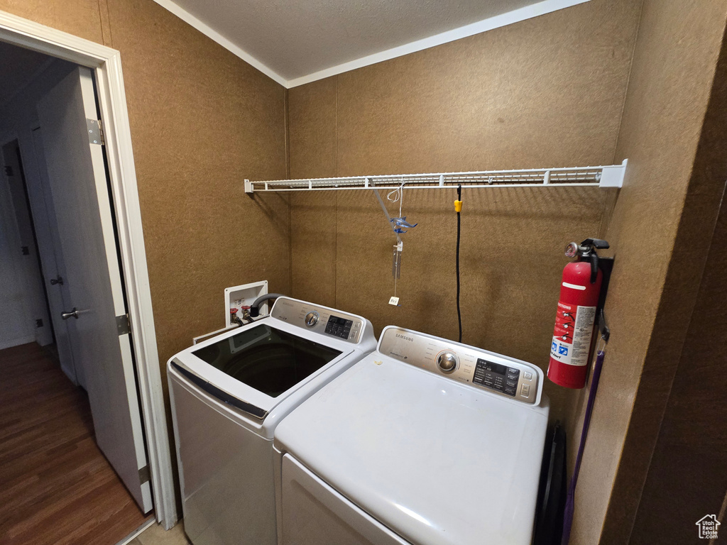 Washroom with a textured wall, laundry area, wood finished floors, and washing machine and clothes dryer