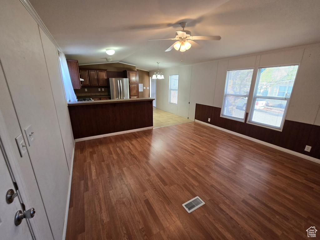 Unfurnished living room with vaulted ceiling, ceiling fan with notable chandelier, wood finished floors, and visible vents