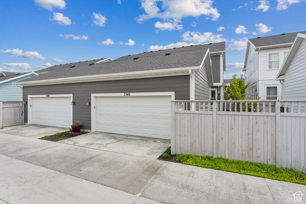View of side of home with a shingled roof, fence, and concrete driveway