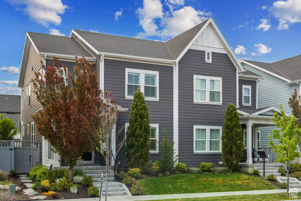 View of front of property featuring a front lawn, a shingled roof, board and batten siding, a porch, and stairway
