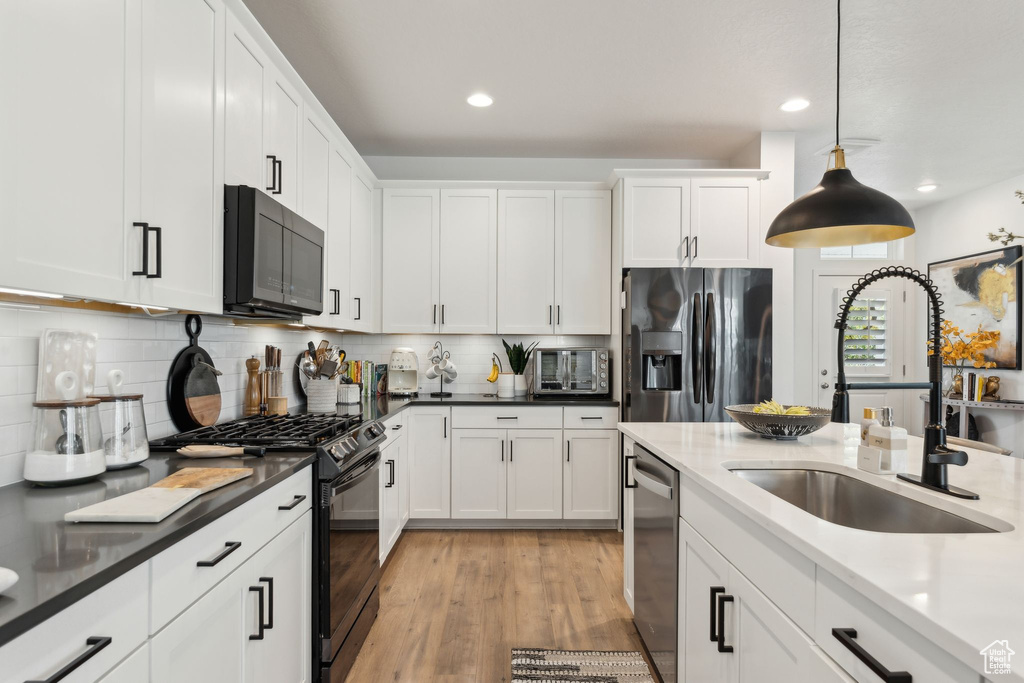 Kitchen featuring recessed lighting, white cabinetry, a sink, black appliances, and hanging light fixtures