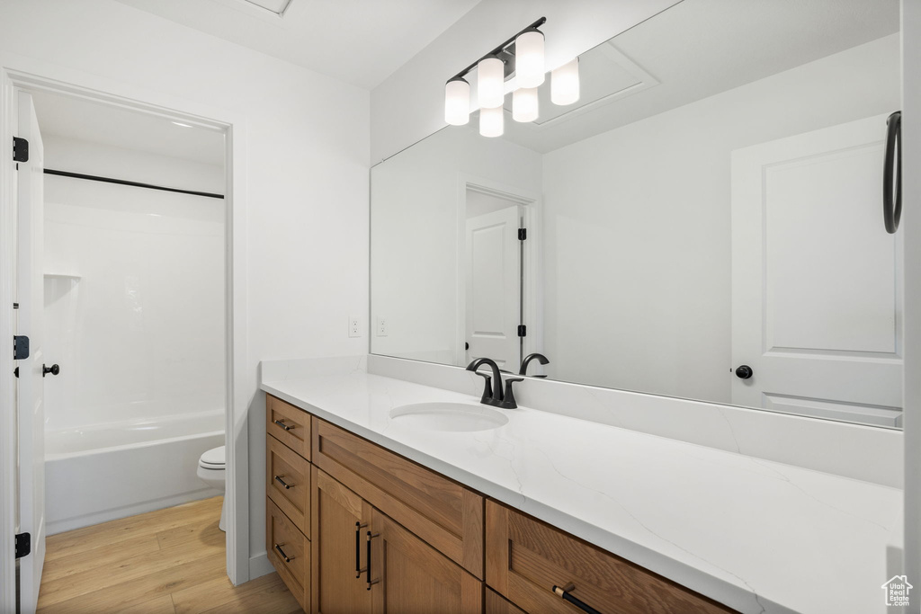 Bathroom with vanity, washtub / shower combination, wood finished floors, and toilet