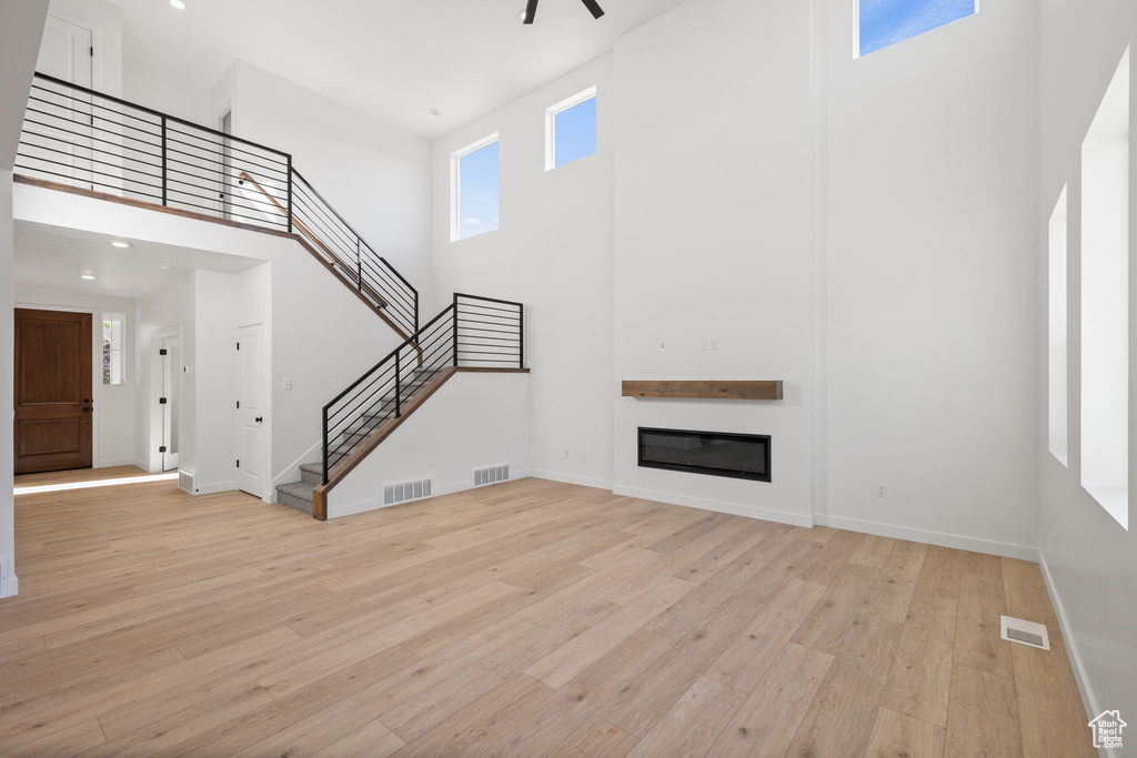Unfurnished living room featuring light wood-style floors, a towering ceiling, and visible vents