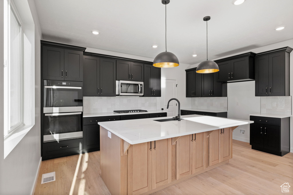 Kitchen featuring backsplash, visible vents, dark cabinets, light wood-style floors, and stainless steel appliances