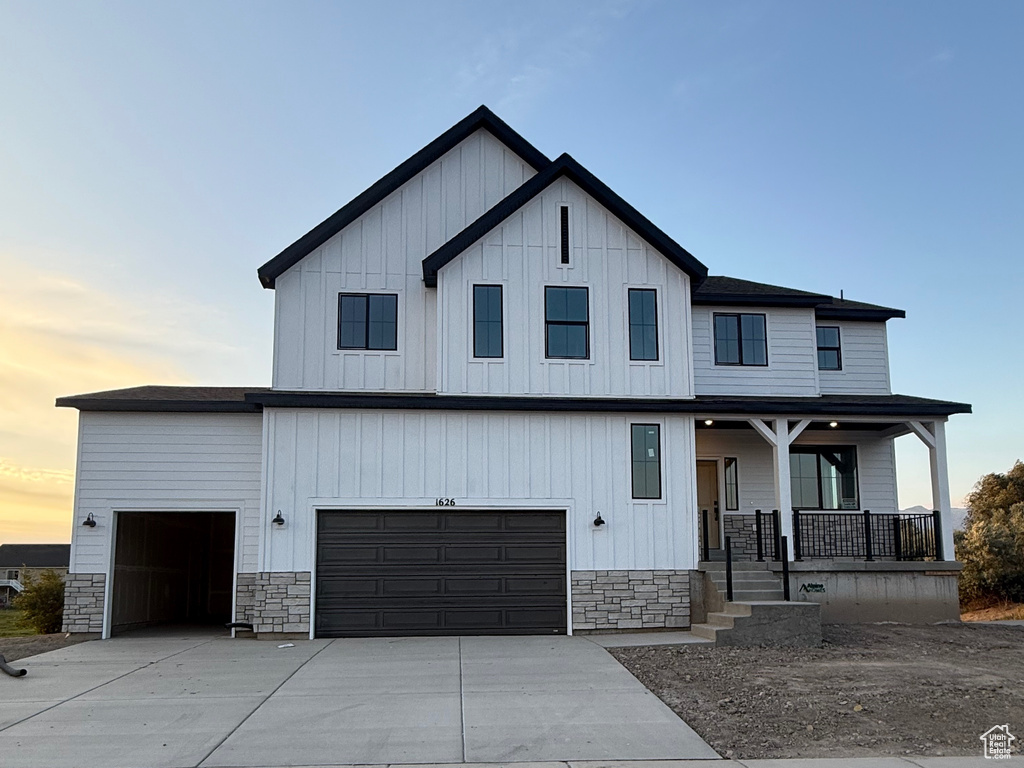 Modern inspired farmhouse with stone siding, board and batten siding, covered porch, and driveway