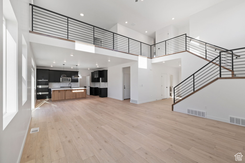 Unfurnished living room featuring visible vents, a towering ceiling, and stairway