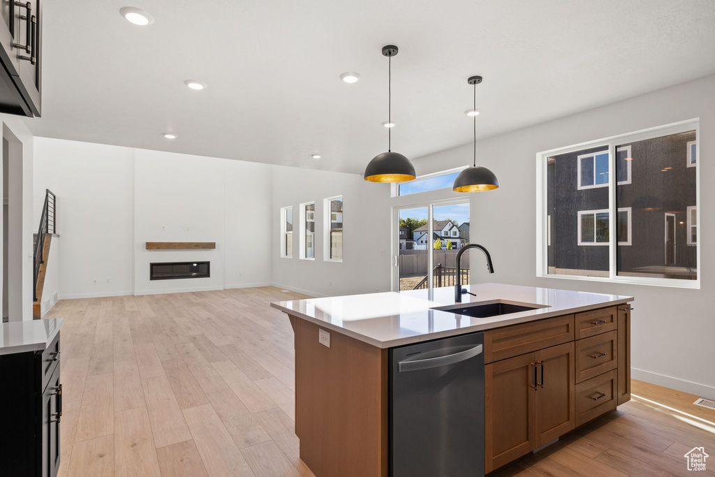 Kitchen with a sink, dishwasher, light countertops, light wood-type flooring, and a center island with sink