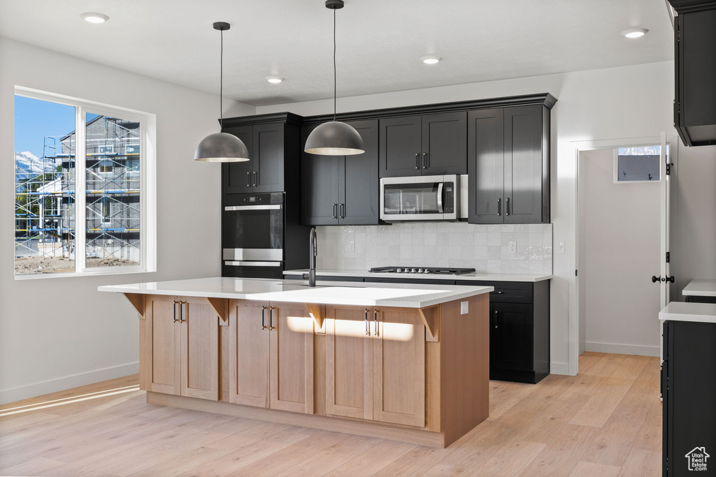 Kitchen with tasteful backsplash, light wood-type flooring, light countertops, baseboards, and stainless steel appliances