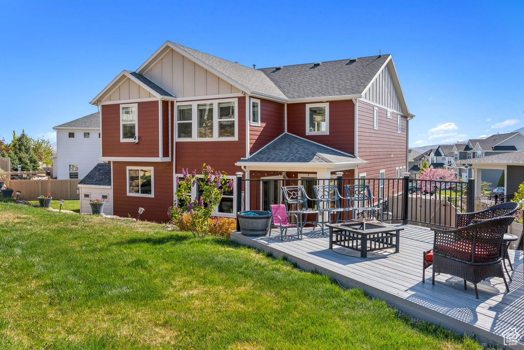 Back of property featuring a shingled roof, board and batten siding, a deck, a yard, and a fire pit