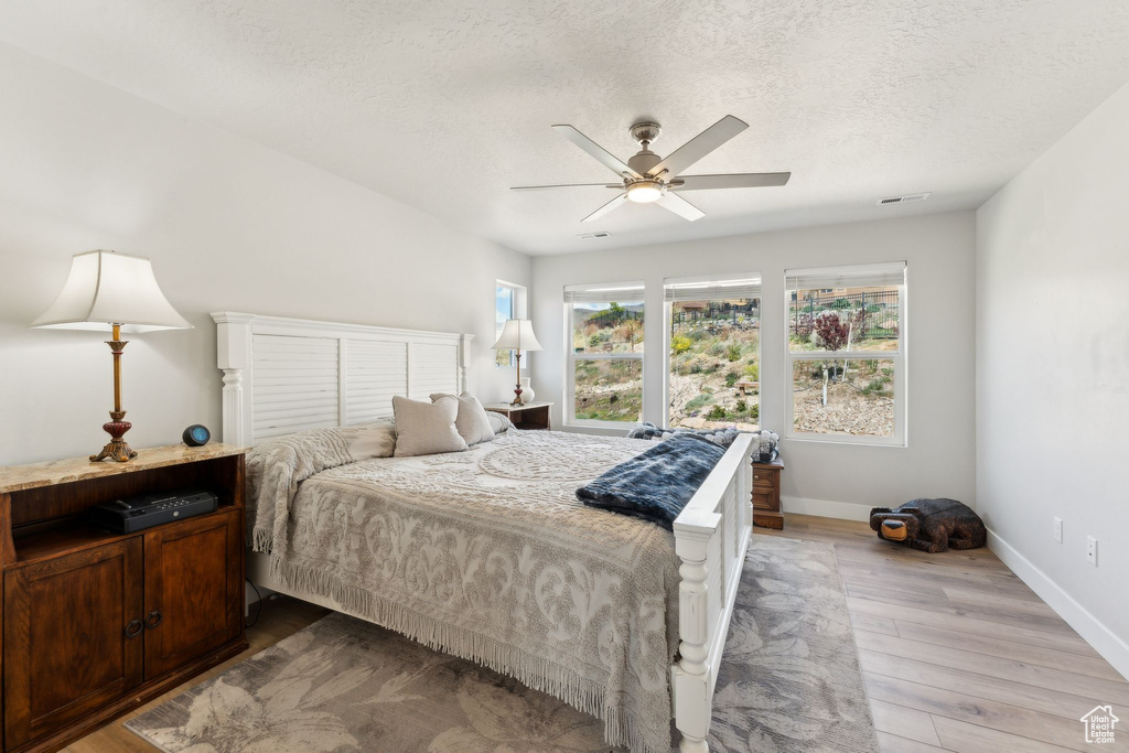 Bedroom featuring baseboards, a textured ceiling, light wood-style flooring, and multiple windows