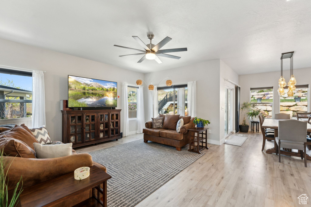 Living area with light wood-style flooring, a wealth of natural light, and ceiling fan with notable chandelier