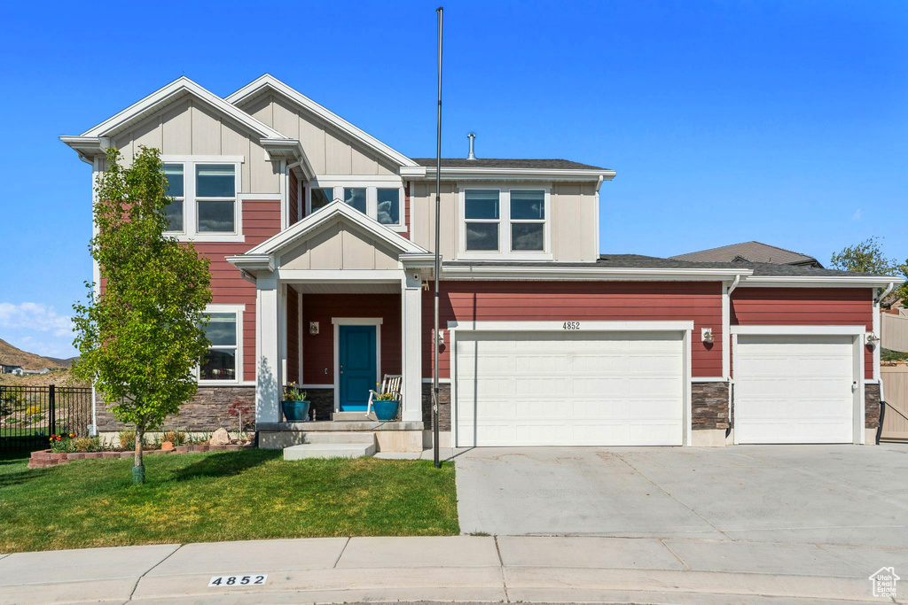 Craftsman-style house with board and batten siding, a front yard, fence, concrete driveway, and stone siding