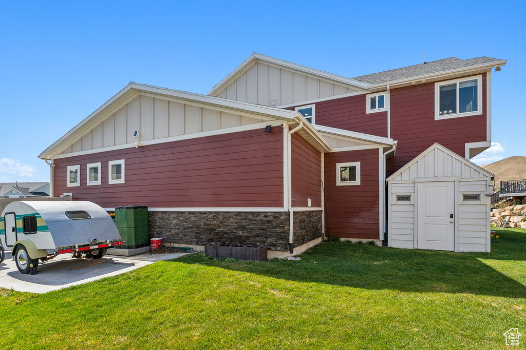 Back of property with a storage shed, board and batten siding, a yard, and stone siding