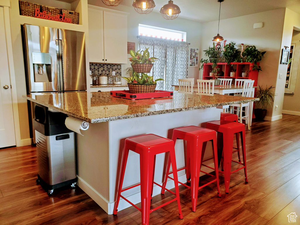 Kitchen with backsplash, pendant lighting, light stone countertops, white cabinets, and dark wood-style floors