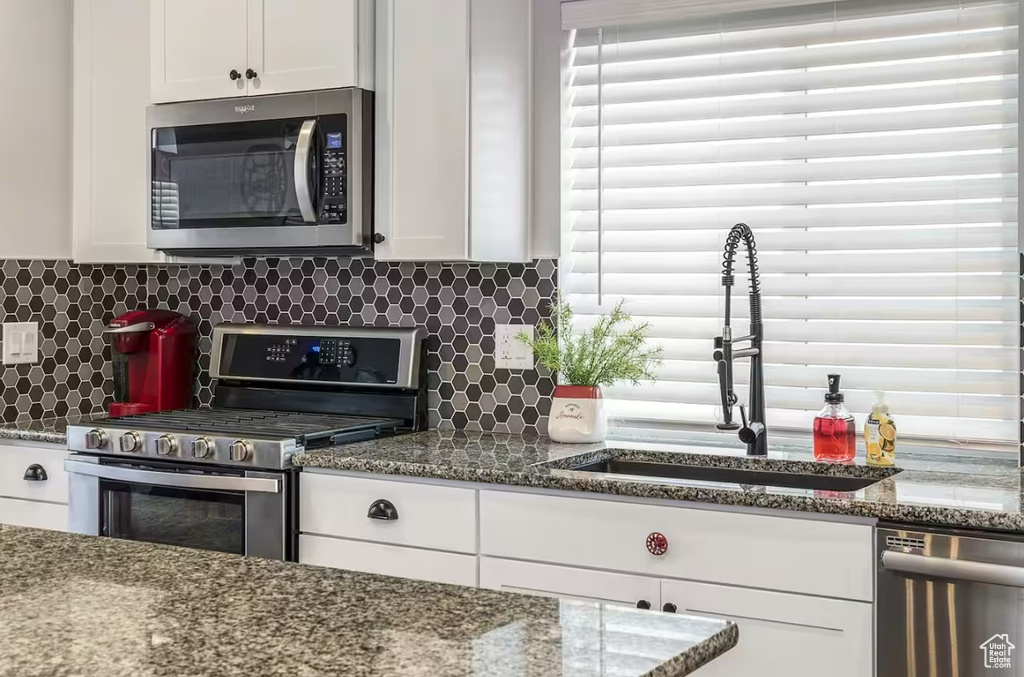 Kitchen with stainless steel appliances, white cabinetry, a sink, and tasteful backsplash