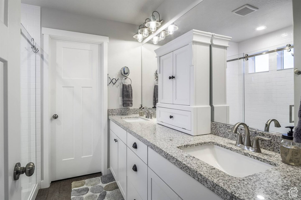 Full bath with double vanity, a tile shower, a sink, and wood finished floors