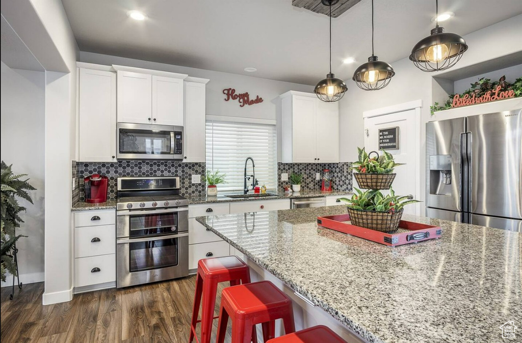 Kitchen with a kitchen breakfast bar, tasteful backsplash, light stone counters, a sink, and stainless steel appliances