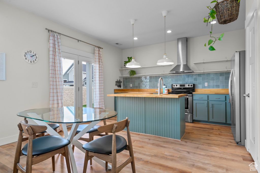 Kitchen with wall chimney range hood, tasteful backsplash, open shelves, stainless steel appliances, and butcher block countertops