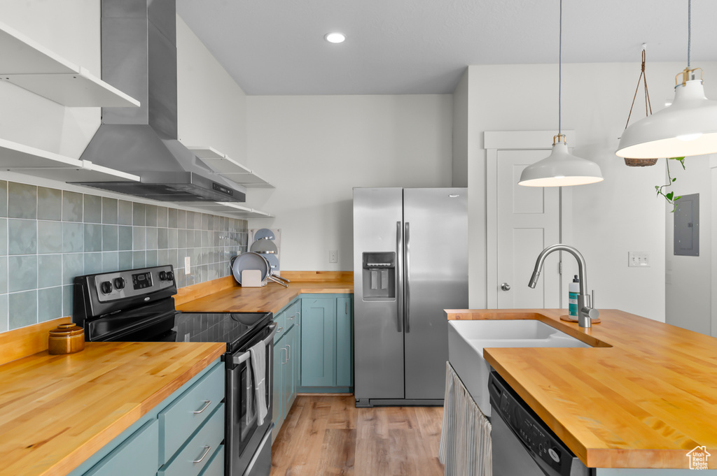 Kitchen with wall chimney range hood, wood counters, open shelves, and appliances with stainless steel finishes