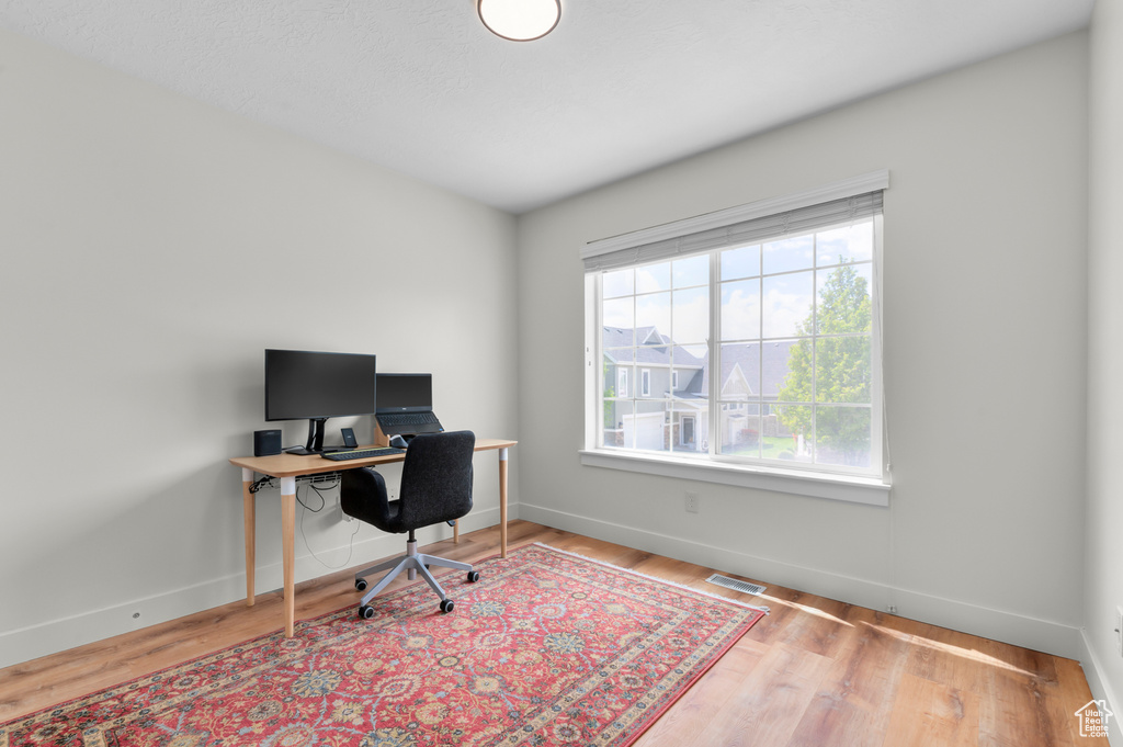 Home office with baseboards, visible vents, and wood finished floors