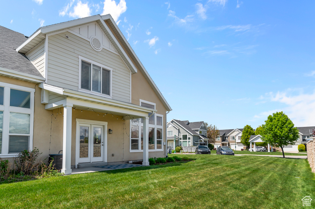 Back of house with stucco siding, french doors, a shingled roof, a yard, and a residential view