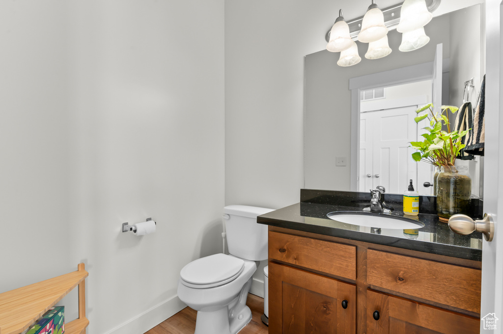 Half bath featuring visible vents, wood finished floors, vanity, baseboards, and toilet