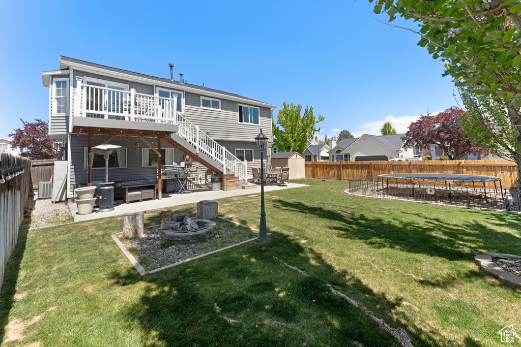 Back of house with a fire pit, a fenced backyard, a shed, stairs, and a trampoline