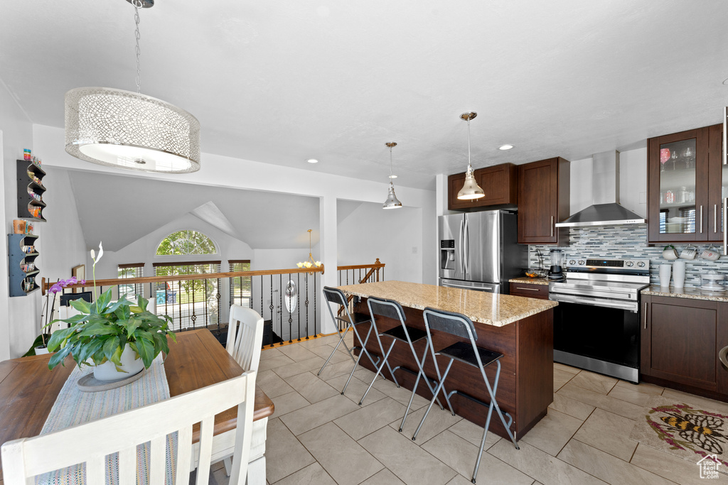 Kitchen featuring decorative backsplash, appliances with stainless steel finishes, light tile patterned floors, glass insert cabinets, and wall chimney exhaust hood