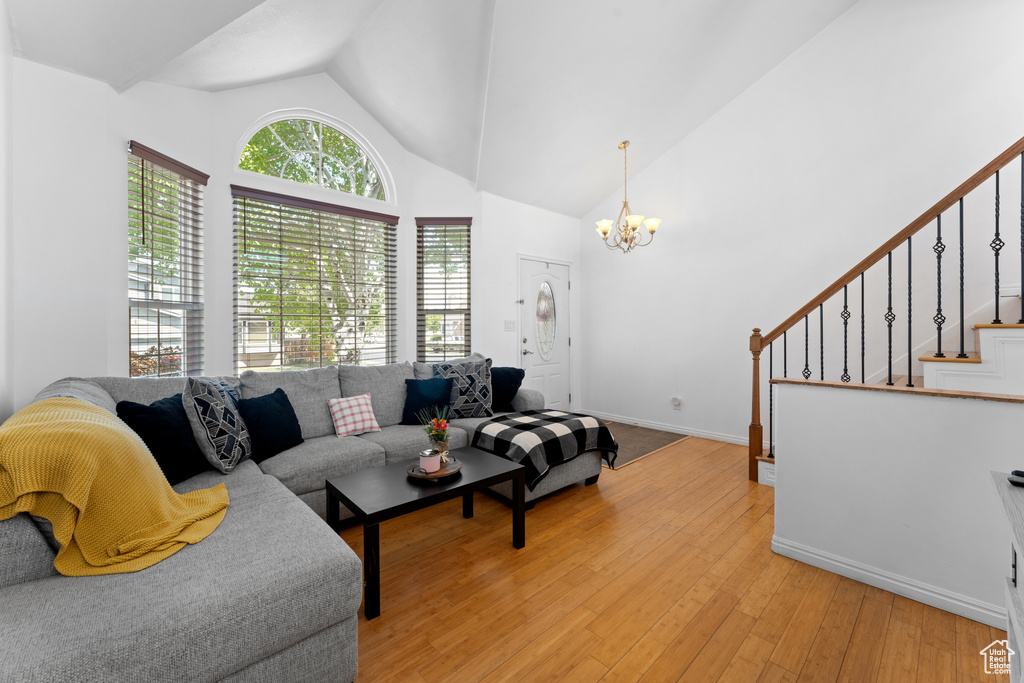 Living area featuring light wood finished floors, a chandelier, stairs, baseboards, and vaulted ceiling
