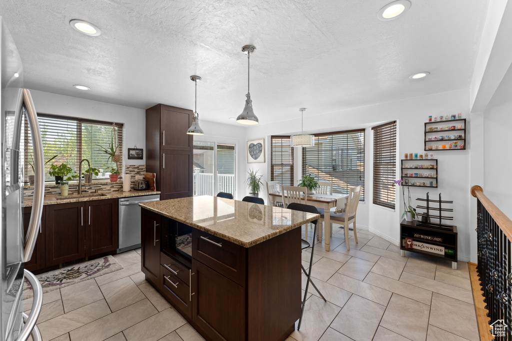 Kitchen with dark brown cabinets, a center island, stainless steel appliances, recessed lighting, and a kitchen bar