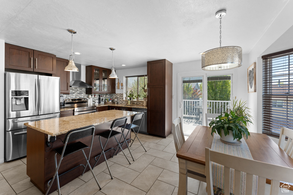 Kitchen with wall chimney exhaust hood, stainless steel appliances, tasteful backsplash, a kitchen island, and glass insert cabinets