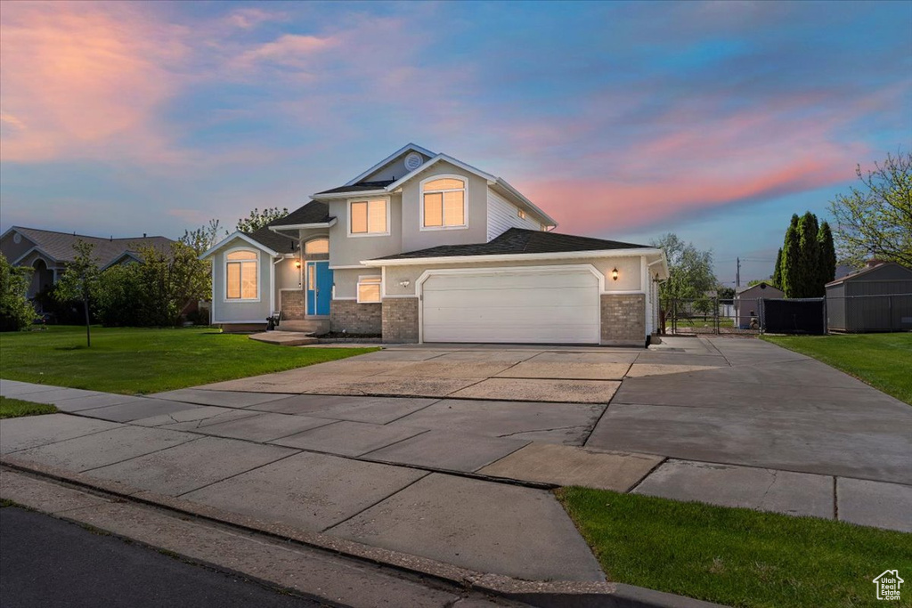 View of front facade featuring driveway, brick siding, fence, a yard, and stucco siding