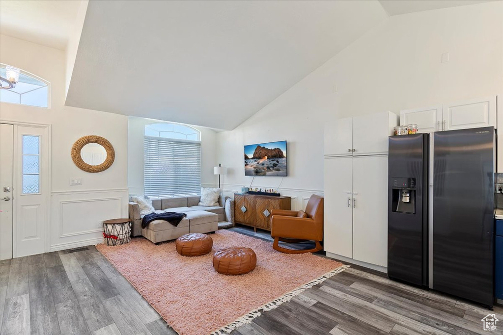 Living room with a decorative wall, high vaulted ceiling, wood finished floors, and a wainscoted wall
