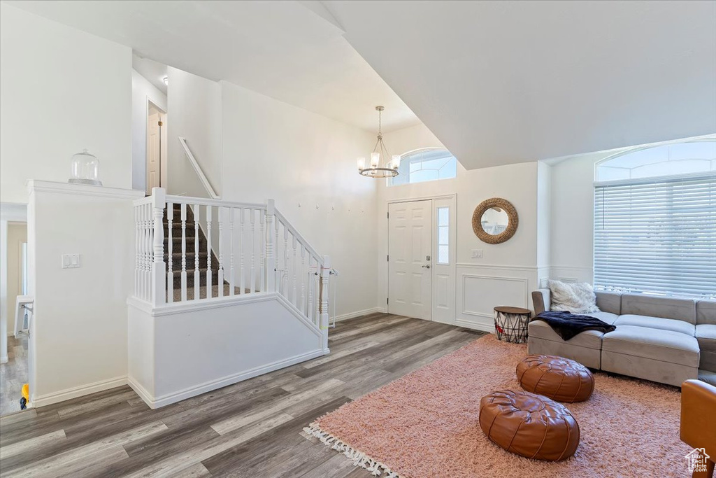 Living area with vaulted ceiling, wood finished floors, baseboards, a chandelier, and stairs