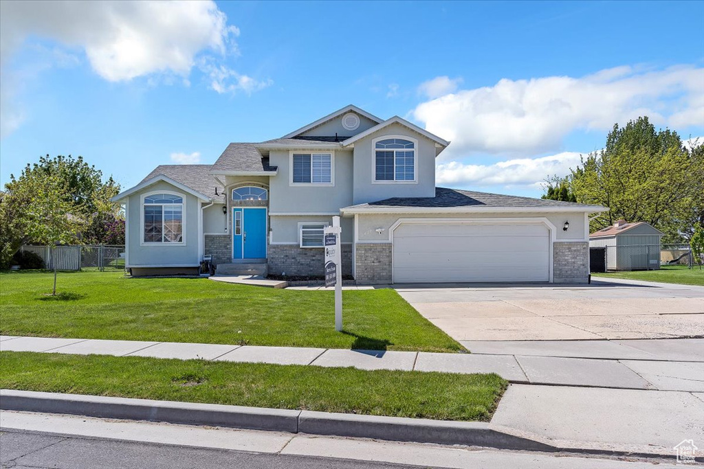 View of front of property featuring a front yard, brick siding, fence, concrete driveway, and stucco siding