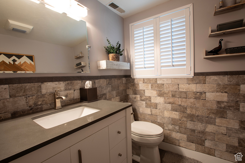 Half bathroom featuring toilet, tile walls, visible vents, and a wainscoted wall