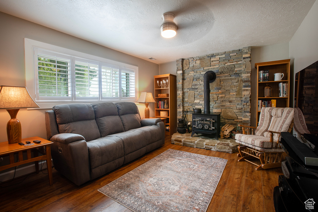 Living room with a ceiling fan, a wood stove, hardwood / wood-style flooring, and a textured ceiling