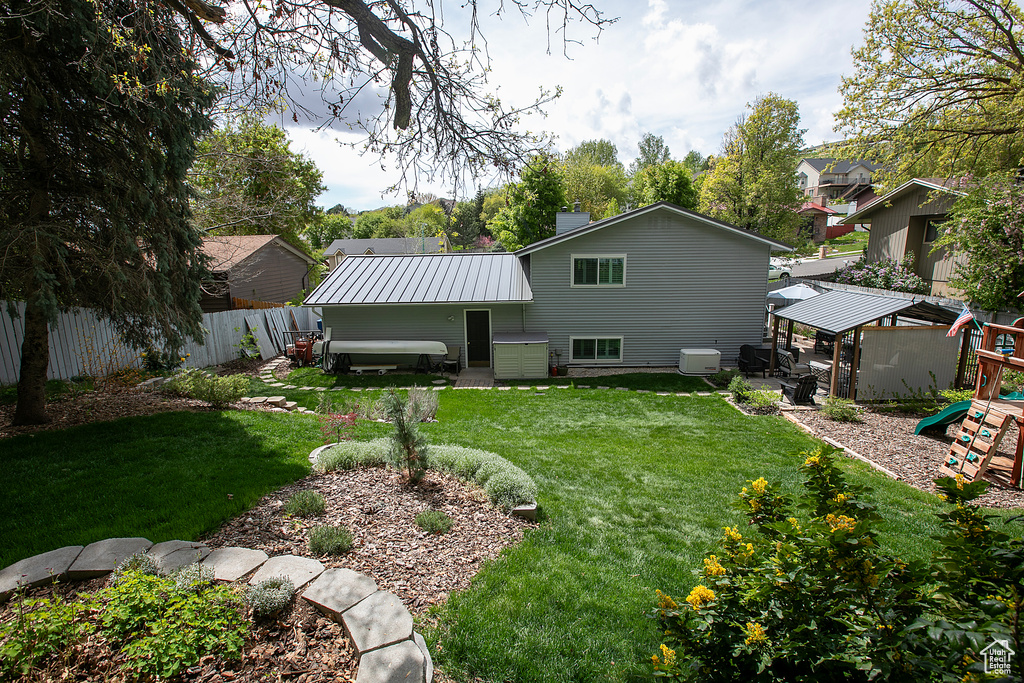 Back of house featuring fence, a gazebo, a playground, a yard, and metal roof