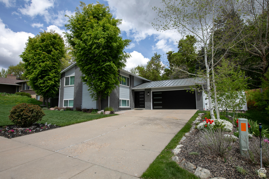 View of front of property with an attached garage, a front yard, concrete driveway, a standing seam roof, and metal roof
