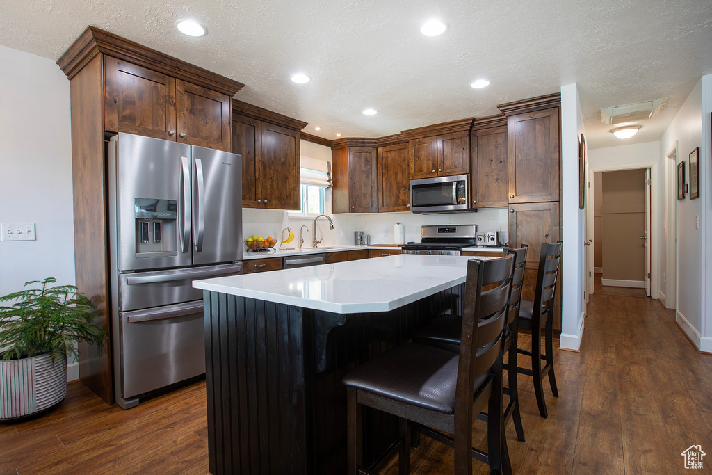 Kitchen with appliances with stainless steel finishes, a kitchen breakfast bar, a kitchen island, and dark wood-style flooring